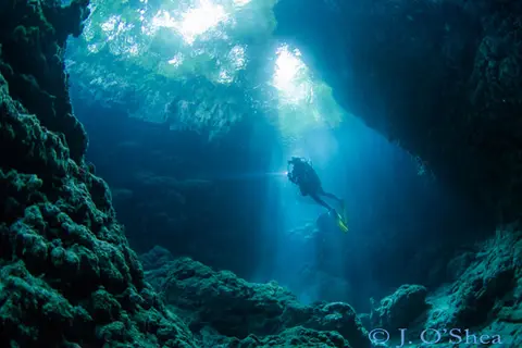 Mbulo Caves in Mbulo Island has a series of caves cut into the reef around the island. This dive is all about the light; swimming in and out of caves, finding beams of light to shoot. A green jungle canopy lies above.