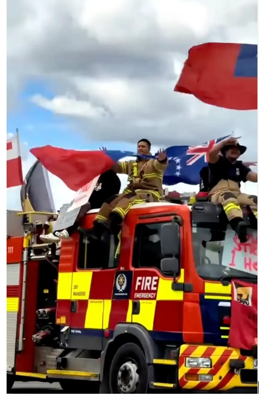 Firefighters on a fire truck draped in Pacific flags during Rugby League World Cup celebrations in Auckland.