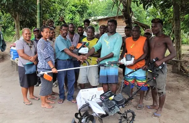 Daniel Ogu Besa’a, Minister of Agriculture & Fisheries of Guadalcanal Province (in green shirt) with two female officers from MAL Guadalcanal Province Extension Office hands over the tools to MK Farm Fresh owner and recipient John Maeli  Kauvera, flanked by his farm workers.